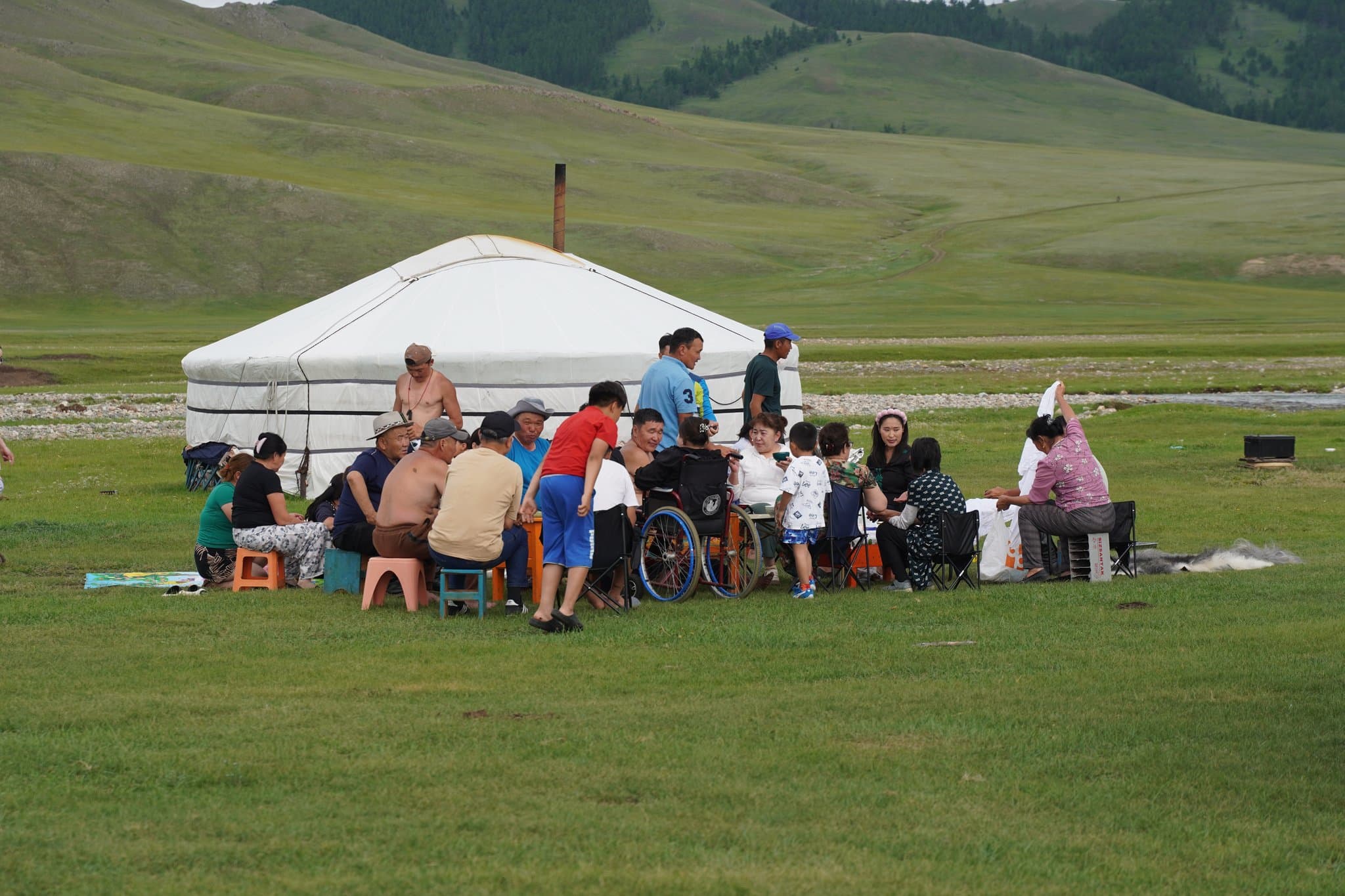 A Mongolian family gathered for a meal beside their ger on the green steppe during Naadam
